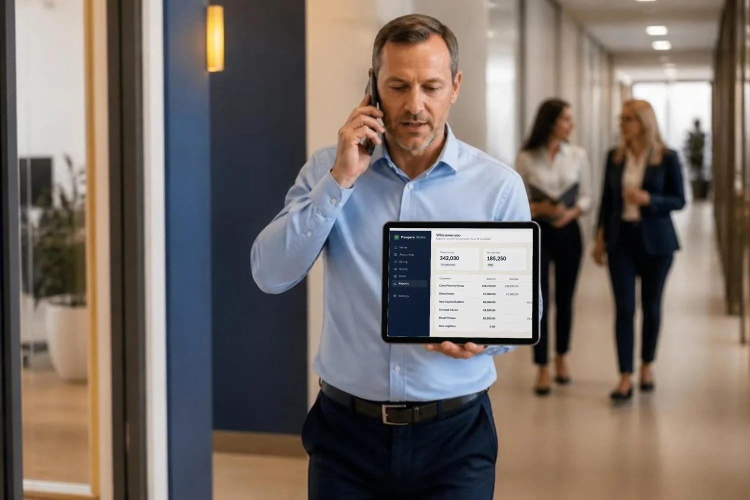 A credit controller on a call walks the office corridor, the receivables report open on his tablet