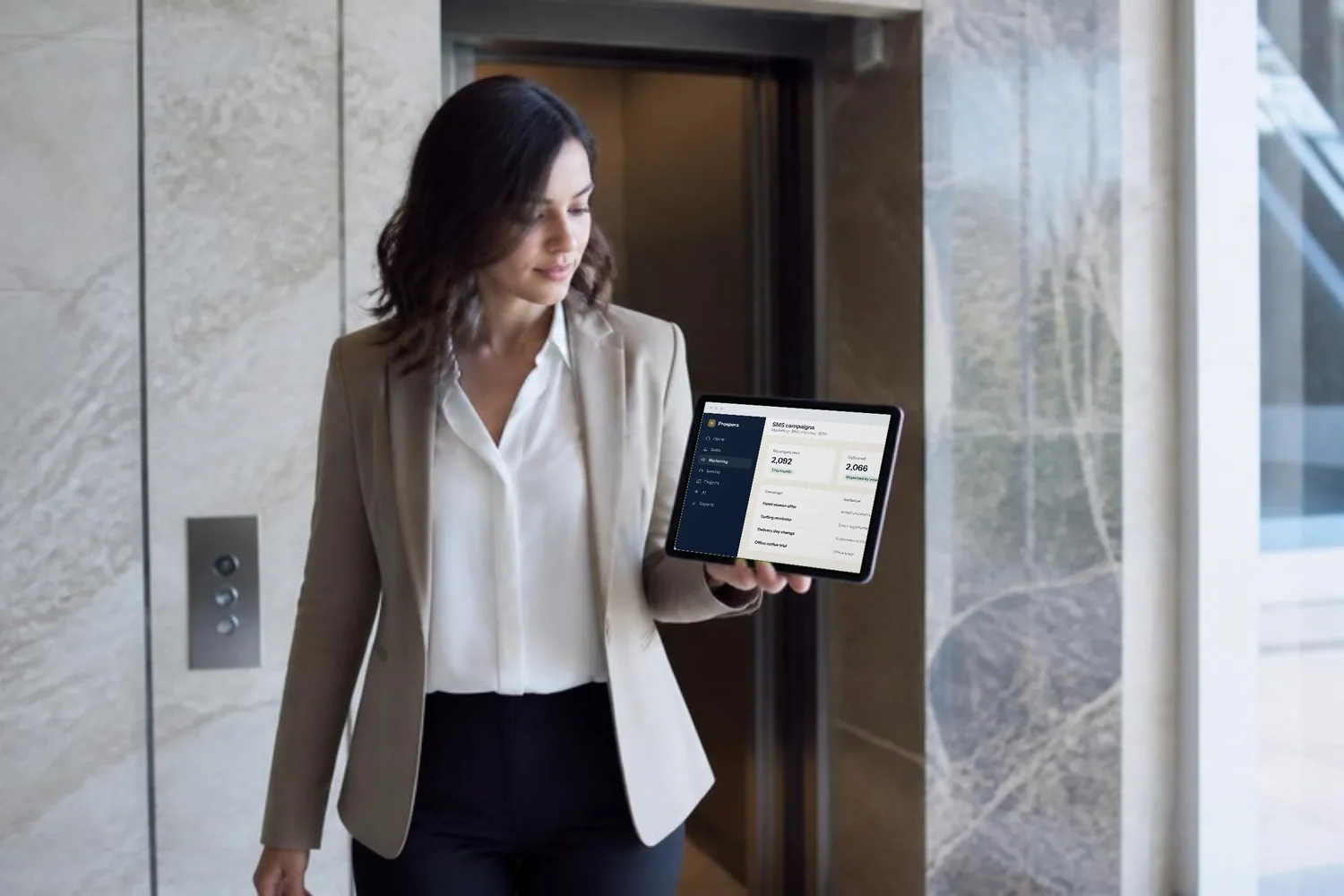 A marketing coordinator steps out of a lift checking an SMS campaign on her phone